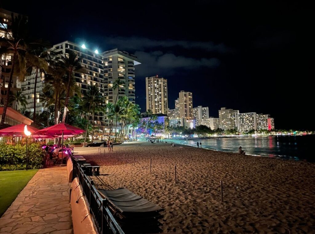 Review & Video: The Royal Hawaiian, Waikiki, A Luxury Collection Hotel Hawaii Calling a beach with buildings and palm trees at night