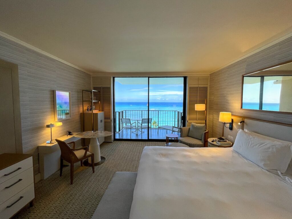 a room with a bed and a table and chairs and a balcony with a view of the ocean