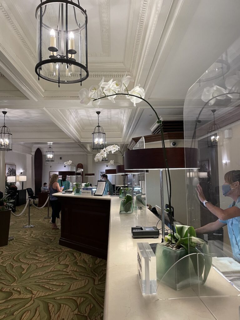 Review & Video: Moana Surfrider, Waikiki Beach Beauty Hawaii Calling a hotel lobby with a white counter and a woman in a mask