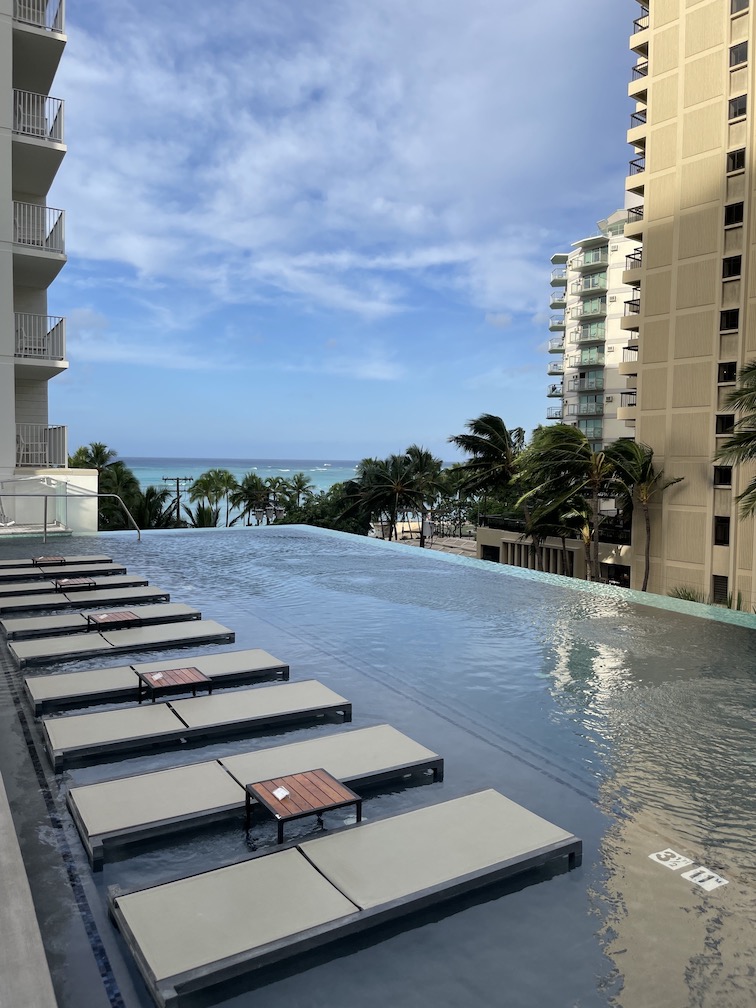 Review & Video: 'Alohilani Resort Waikiki Beach, A Unique Oasis Hawaii Calling a pool with lounge chairs and a beach in the background