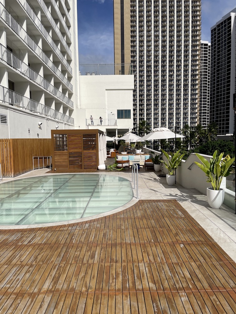 Review & Video: 'Alohilani Resort Waikiki Beach, A Unique Oasis Hawaii Calling a pool with a wood deck and umbrellas in front of a building