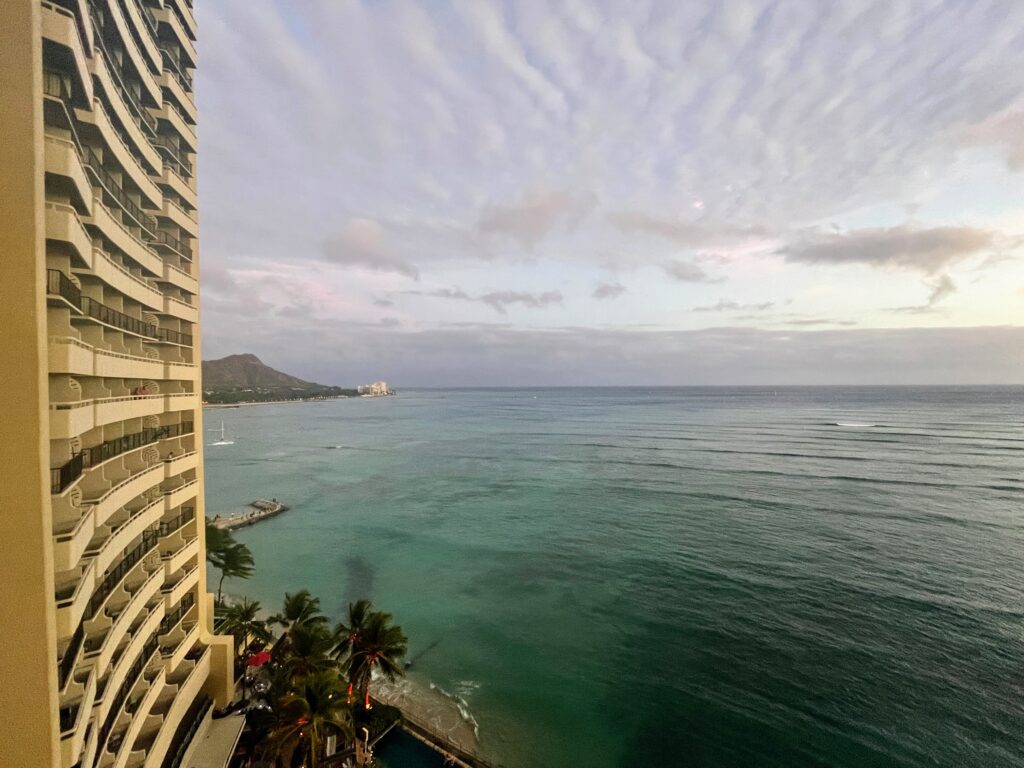 5 Key Features To Know When Deciding Between The Sheraton Waikiki Vs. Royal Hawaiian Hotel Hawaii Calling a view of a beach and a building from a balcony