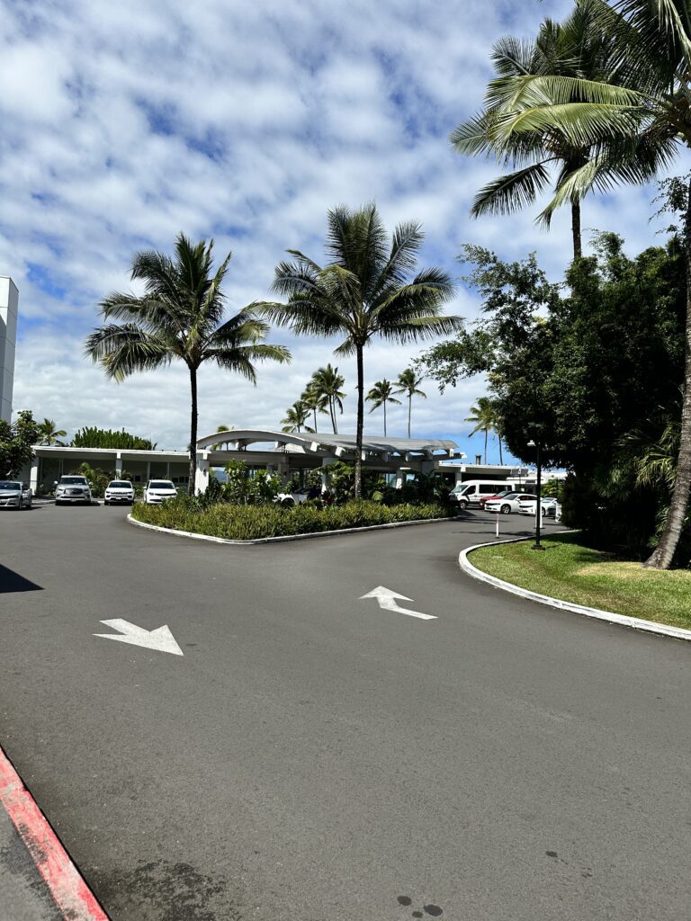 5 Best Budget Friendly Hotels in Hawaii for (2025) Hawaii Calling a road with palm trees and cars on the side leading to the Grand Naniloa Hotel