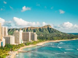 a beach with buildings and a body of water with Diamond Head in the background