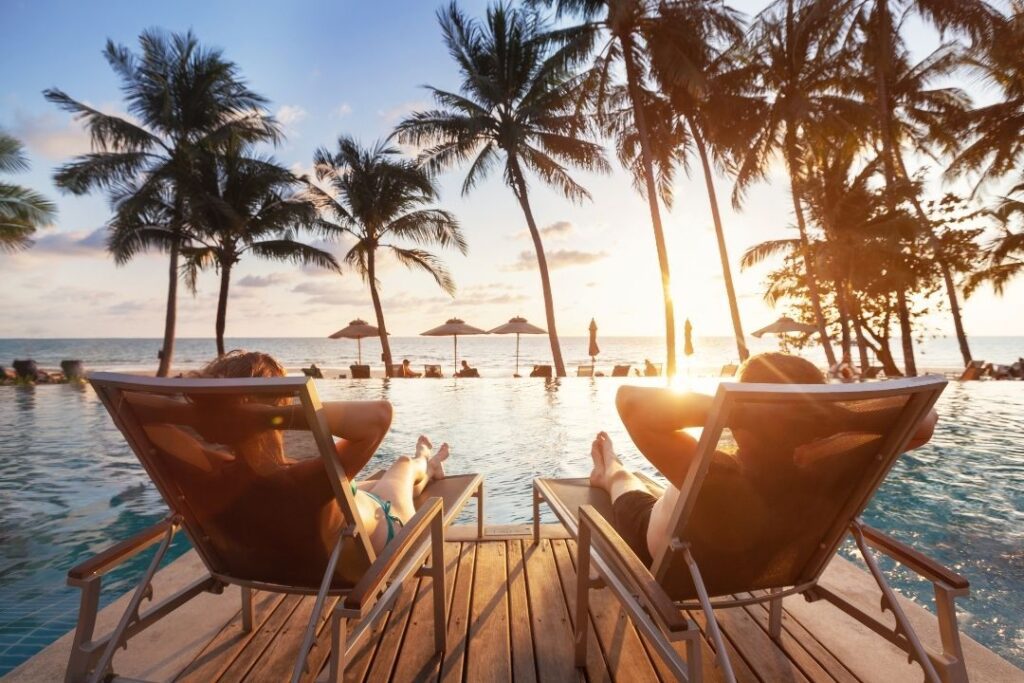 Virtuoso Travel: A Guide To Exclusive Perks & Benefits Hawaii Calling Couple lounging by pool enjoying Virtuoso VIP Perks and amenities.
