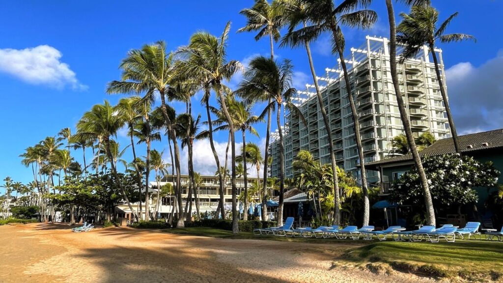 The 15 Best Hotels On Oahu For Families 2025 Hawaii Calling a beach with palm trees and a building