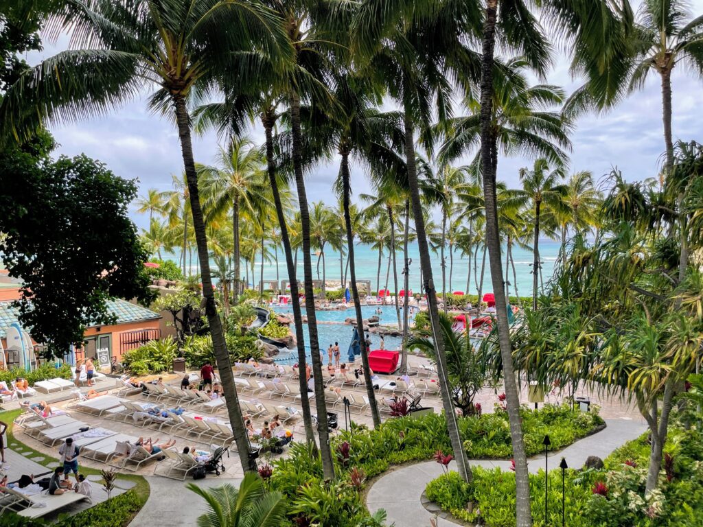 5 Key Features To Know When Deciding Between The Sheraton Waikiki Vs. Royal Hawaiian Hotel Hawaii Calling a pool with palm trees and people in it