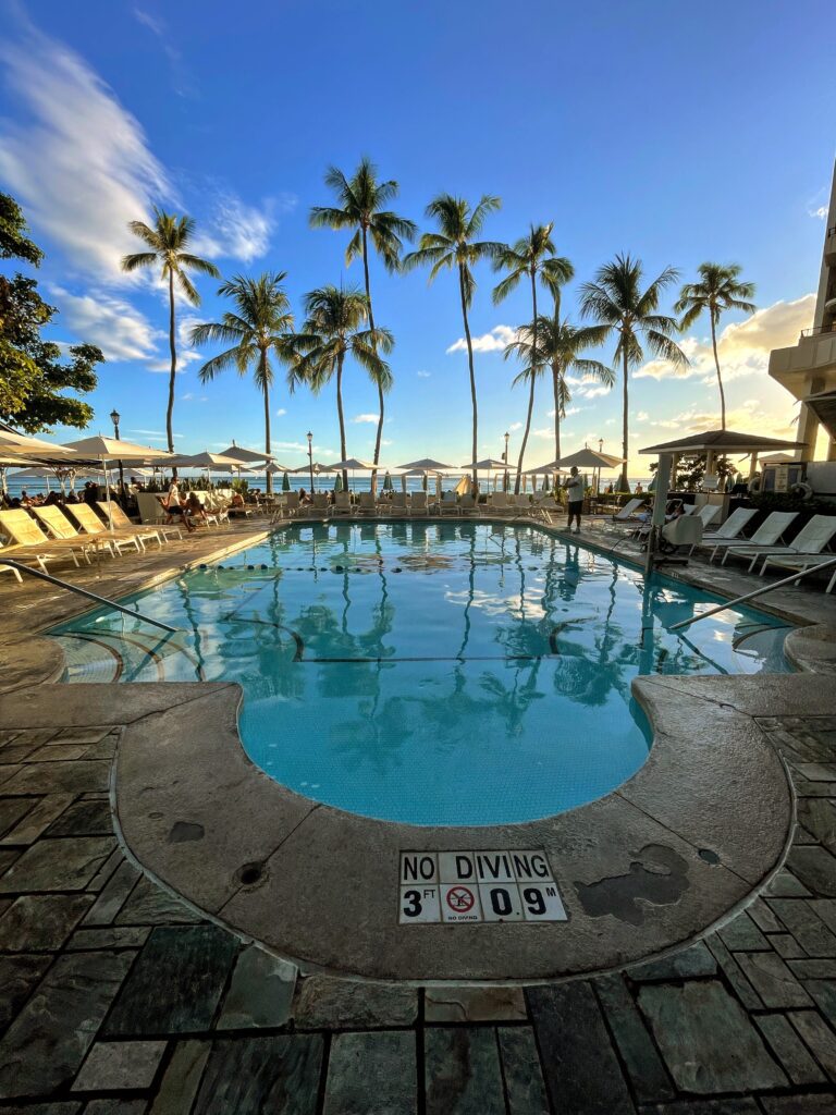 Legendary Sheraton Waikiki Vs. Moana Surfrider | 6 Things to Consider Hawaii Calling a pool with palm trees and umbrellas