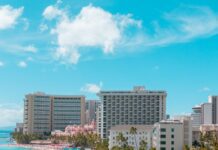 Best Places To Stay In Hawaii (2025)| A Hotel & Island Guide a beach with palm trees and buildings