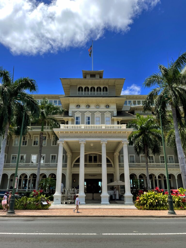 The 23 Best Things To Do In Waikiki |A Local Guide (2025) Hawaii Calling a large building with columns and a flag on top with Iolani Palace in the background