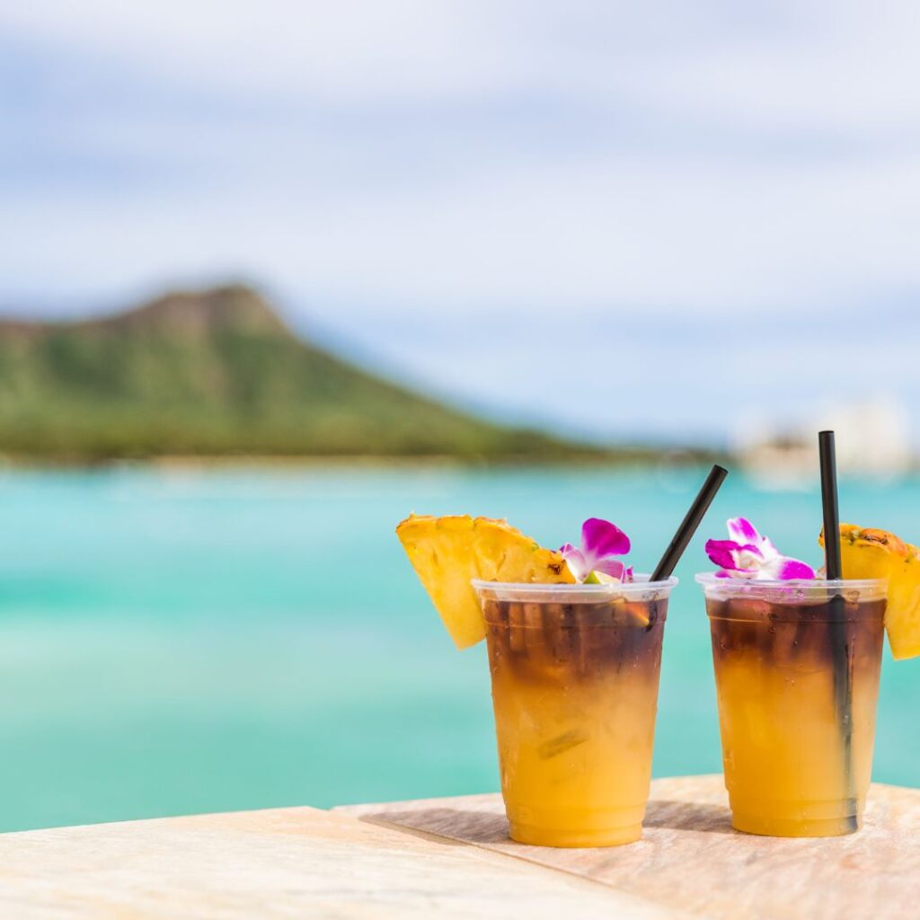 The 23 Best Things To Do In Waikiki |A Local Guide (2025) Hawaii Calling two glasses of liquid with flowers and pineapples on a table