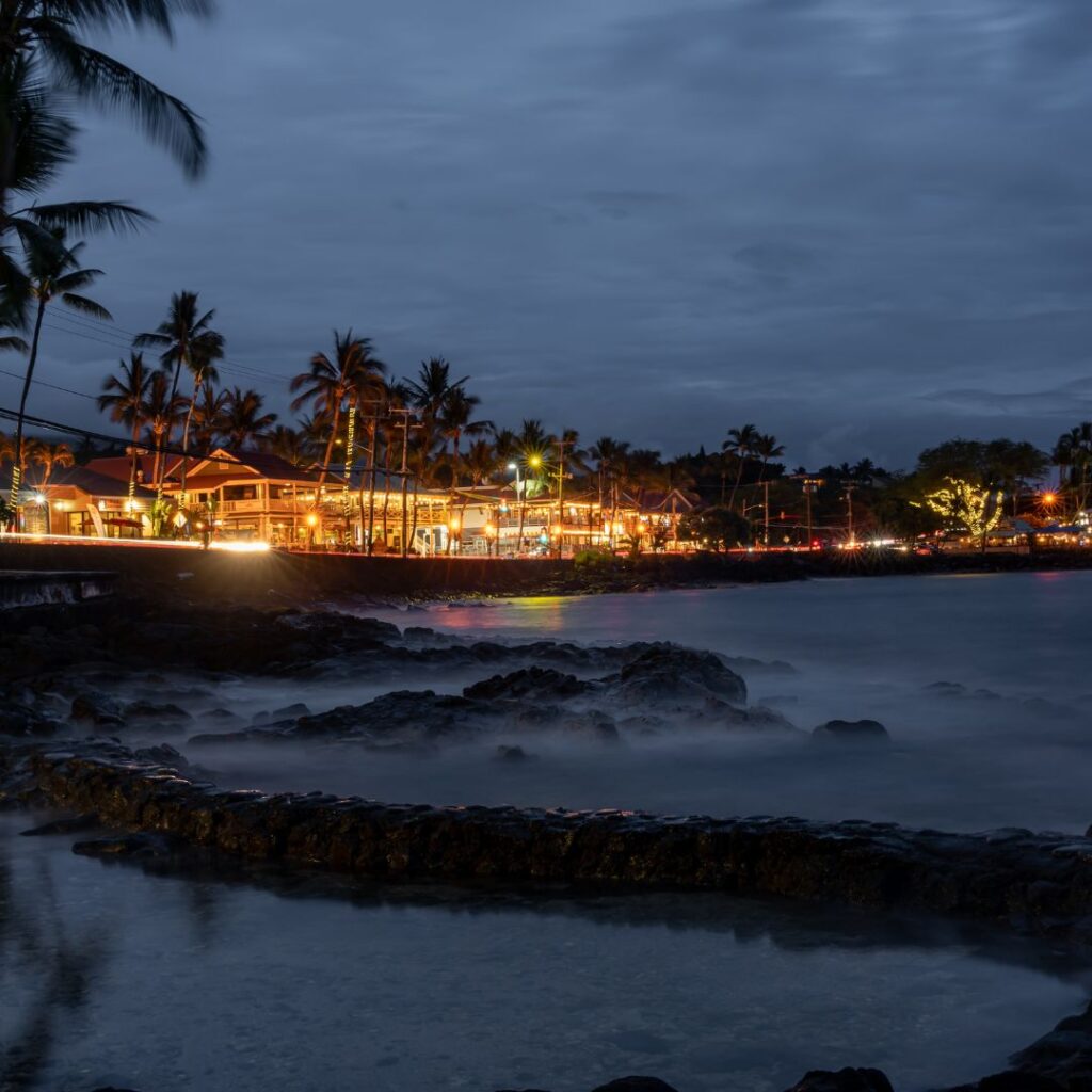 The 49 Best Things To Do In Kona Hawaii Calling a beach with palm trees and buildings at night