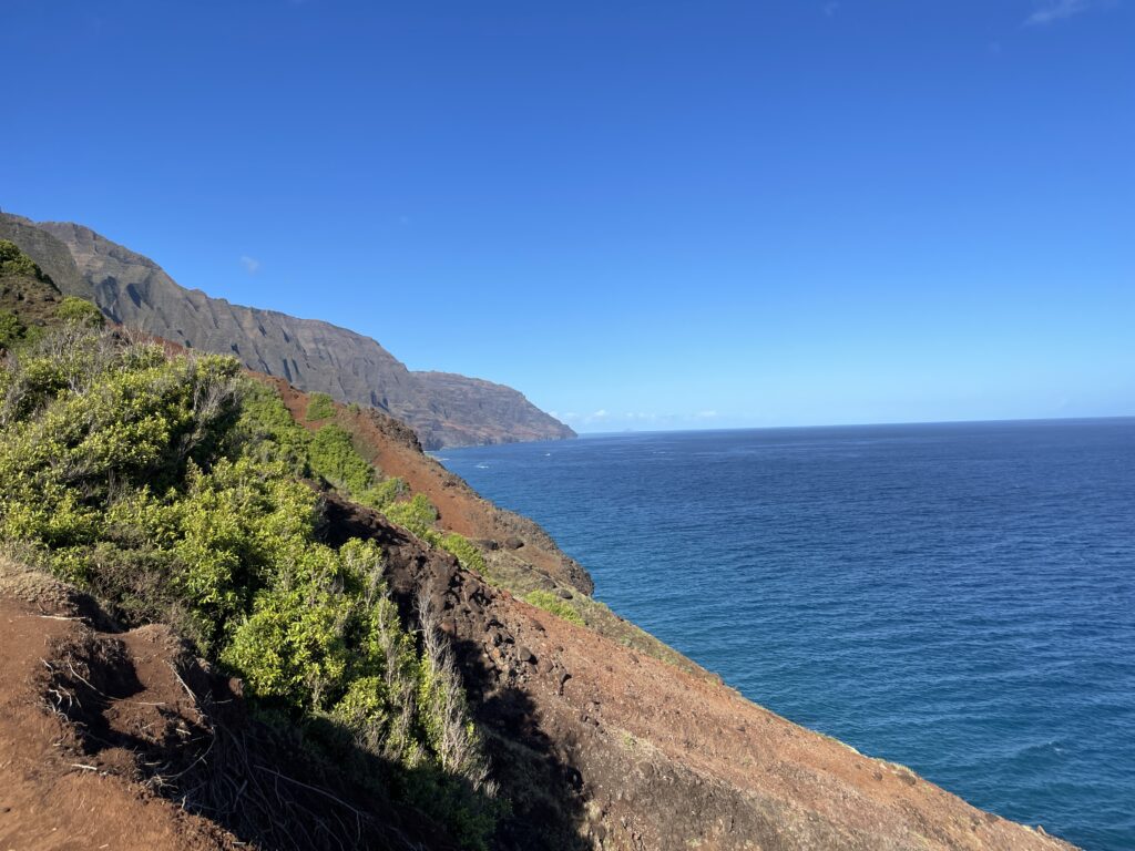 Kalalau Trail Adventure: My Unforgettable Hiking Experience on Kaua'i Hawaii Calling a cliff with a body of water and a blue sky