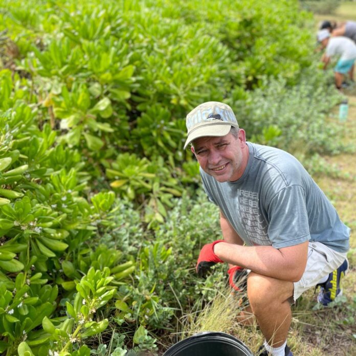 a man kneeling in a field with a bucket of plants