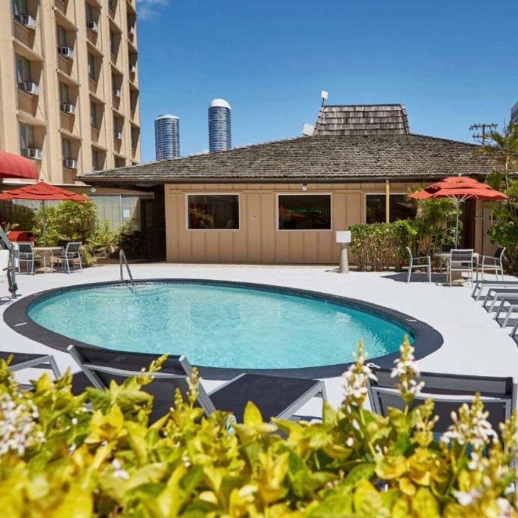 20 Best Budget Hotels On Oahu (2025) Comfort and Convenience for Every Wallet Hawaii Calling a pool with chairs and umbrellas in front of a building
