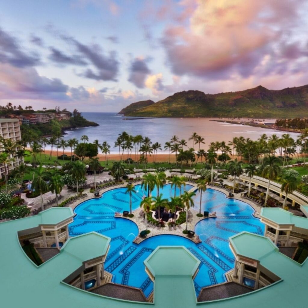12 Best Family Hotels On Kaua'i for a Dream Hawaiian Vacation Hawaii Calling a pool with palm trees and a beach and mountains in the background