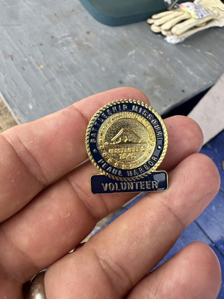 Volunteering At The Battleship Missouri Memorial | Amazing History Behind The Scenes Hawaii Calling a hand holding a gold and blue volunteer badge