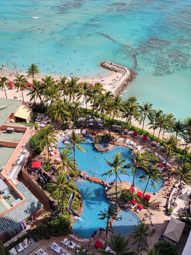 15 Best Beachfront Hotels On Oahu (2025) | Waterfront Bliss Hawaii Calling a swimming pool with palm trees and people on the beach