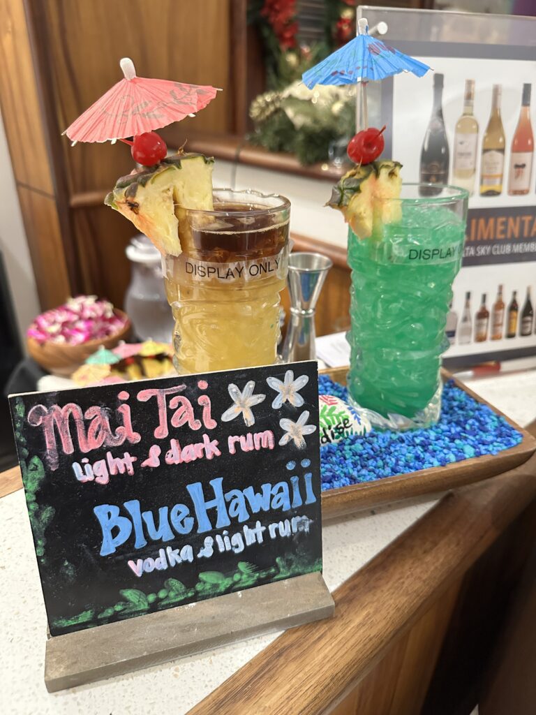 Delta Sky Club Honolulu | Guide & Review (2025) Hawaii Calling a drink with an umbrella and a sign on a tray at the Delta Sky Club Honolulu