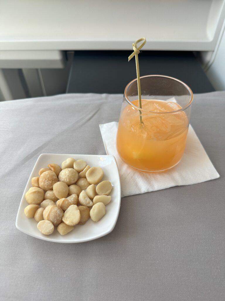 A First Class Experience on Hawaiian Airlines Boeing 787 Dreamliner | Leihōkū Suites | HNL-SFO Hawaii Calling a plate of food and a drink on a napkin