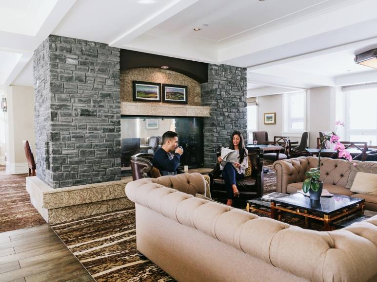 Fairmont Gold Explained: Unlock the Secrets of This Exclusive ‘Hotel Within a Hotel Hawaii Calling a man and woman sitting in a room with a fireplace and stone fireplace