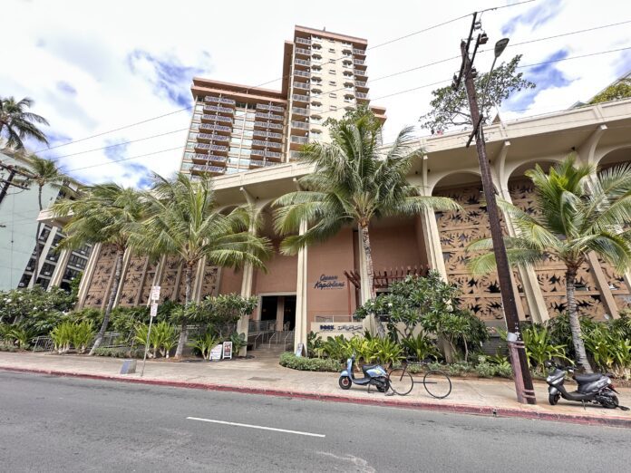 front of the Queen Kapiolani Hotel in Waikiki with palm trees and a street