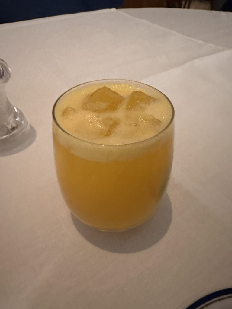 a glass of orange liquid with ice cubes