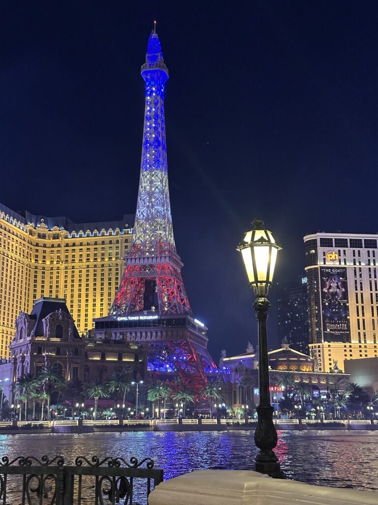 a tall tower with lights and a street lamp in front of a city